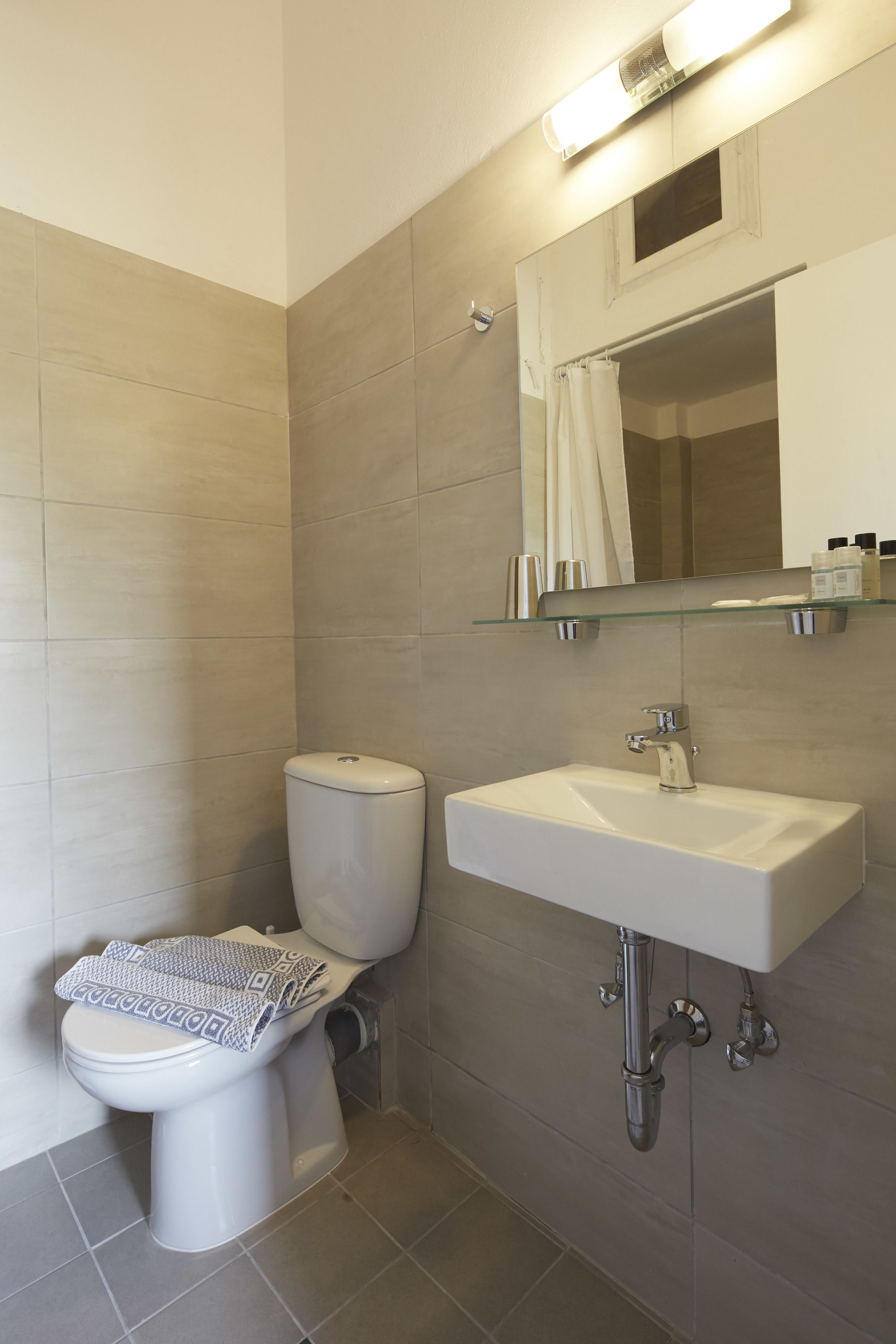 Un baño moderno con inodoro, lavabo y repisa de vidrio sobre el lavabo.