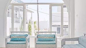A bright room with a large arched window, two chairs with teal cushions, a white table, and a sofa with a light blue cushion. - Londos (Paros)