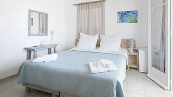 Een slaapkamer met een bed, nachtkastje, spiegel, raam met gordijnen en een deur.