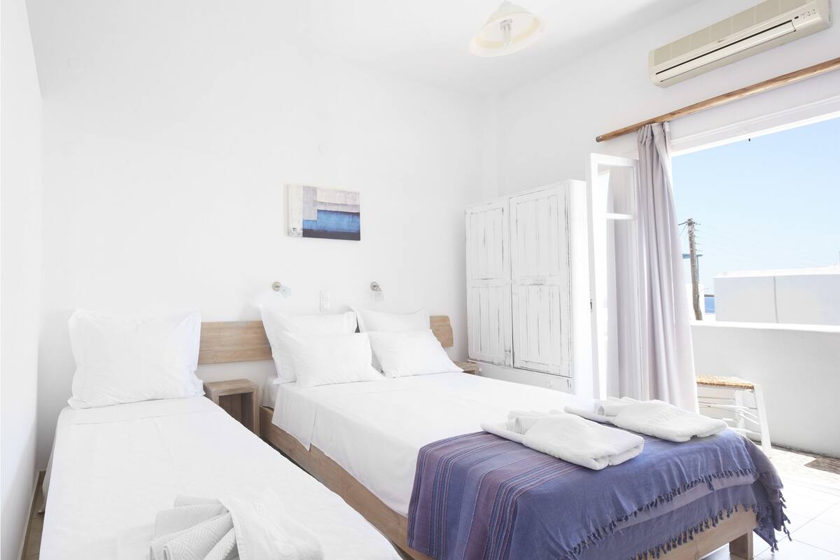 Habitación de hotel con dos camas, una ventana con cortinas, un equipo de aire acondicionado y una pequeña mesa con una silla.