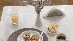 A table set with a plate of pastries, a glass of orange juice, a small bowl of fruit, a cup of coffee, and a vase with dried flowers. - Londos (Paros)
