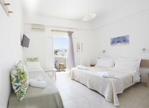 A hotel room with a bed, a bedside table, a TV, and a view of the outside. - Londos (Paros)