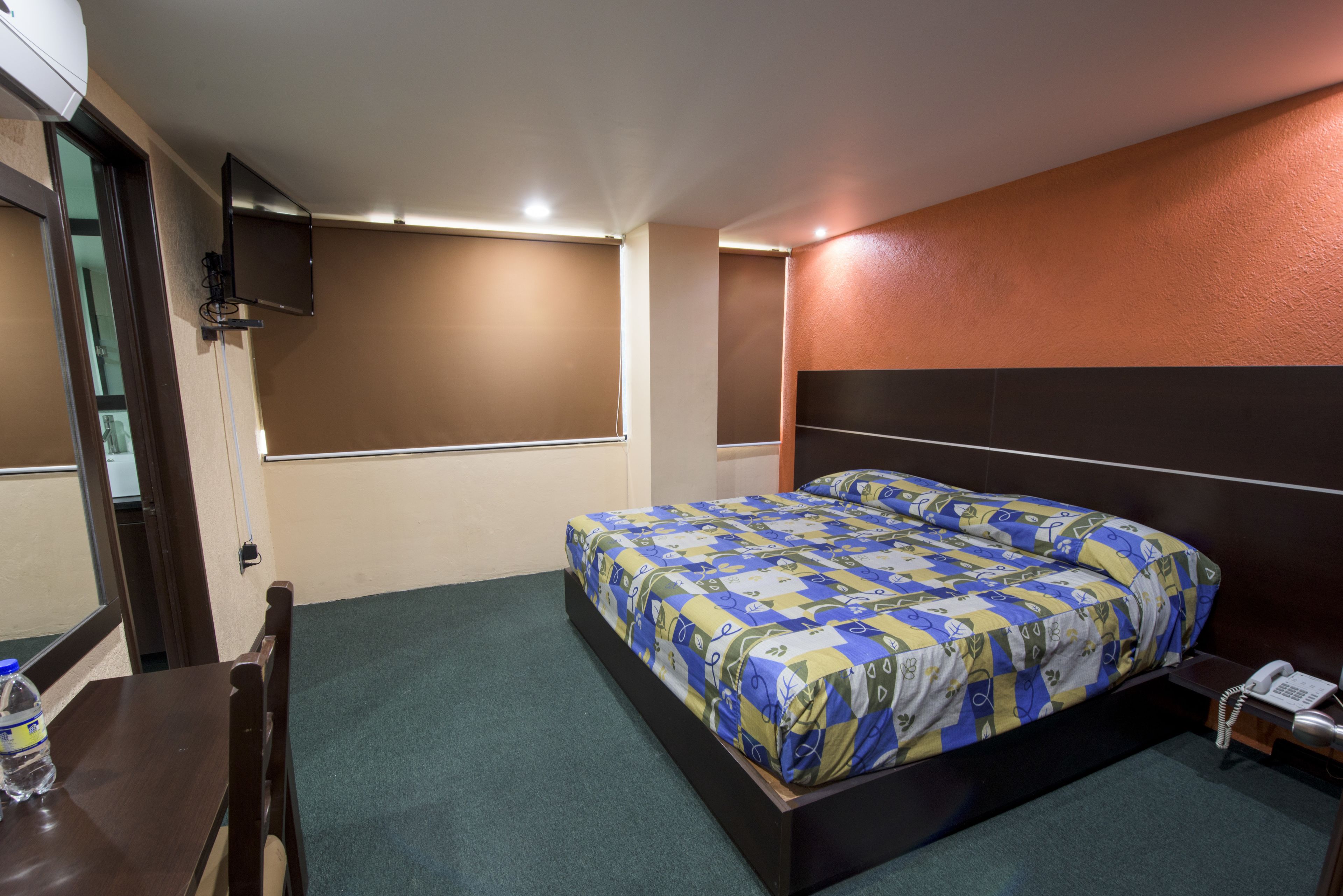 Ein Hotelzimmer mit Bett, Schreibtisch, Stuhl, Telefon und einem an der Wand befestigten Fernseher.