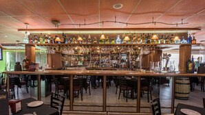A bar area with a variety of liquor bottles and glasses on shelves, a counter with a cash register, and several tables with chairs for dining. - Hotel Oaxaca Inn Reforma (Oaxaca)