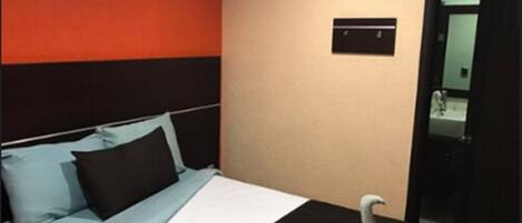 A hotel room with a bed, a wall-mounted air conditioner, and a door leading to a bathroom.