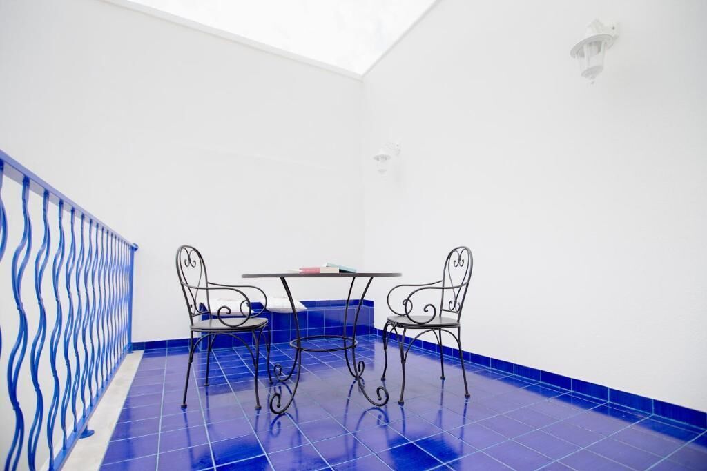 A room with a blue tiled floor, a white wall, a metal railing, and a table with two chairs.
