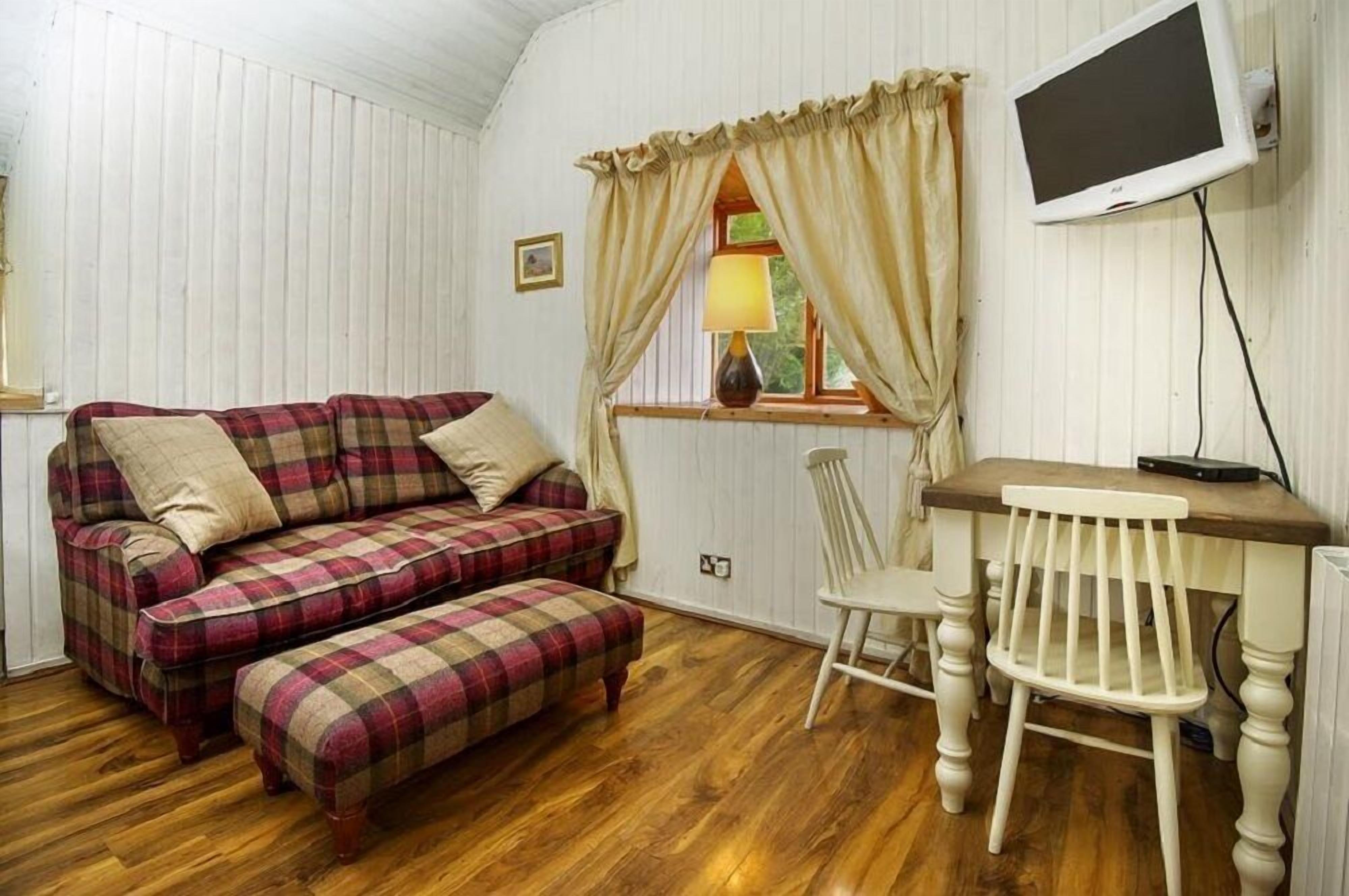 A room with a plaid sofa, a wooden table, a chair, and a television mounted on the wall.