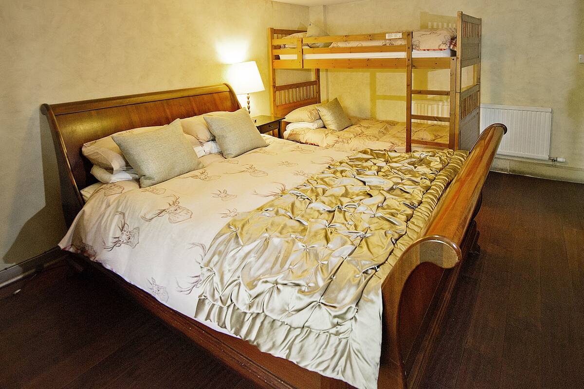 A room with a large bed, a wooden bunk bed, a nightstand with a lamp, and a radiator.