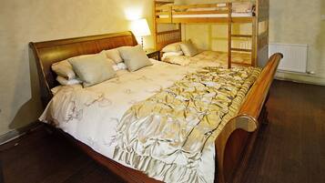 A room with a large bed, a wooden bunk bed, a nightstand with a lamp, and a radiator.