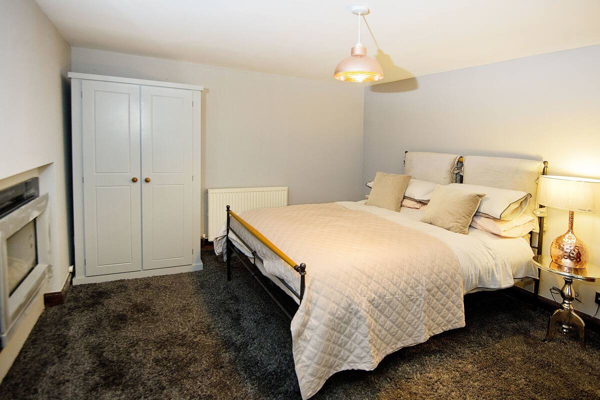 A bedroom with a bed, a wardrobe, a radiator, a lamp, and a carpeted floor.