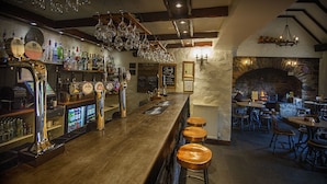 Zona de bar con mostrador de madera, taburetes y pared de piedra con chimenea.