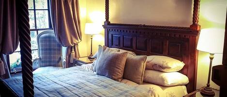 Una cama con dosel, un edredón acolchado, dos lámparas de noche y una silla en una habitación con ventana y cortinas.