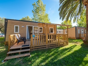 A wooden mobile home with a deck, a sliding door, and a window.