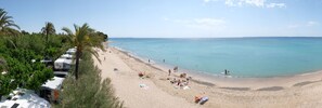 A beach with RVs parked along the shore, clear blue water, and palm trees.