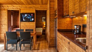 A wooden cabin interior with a dining area, kitchen, and a TV mounted on the wall. - Playa Montroig Camping Resort (Mont-roig del Camp)