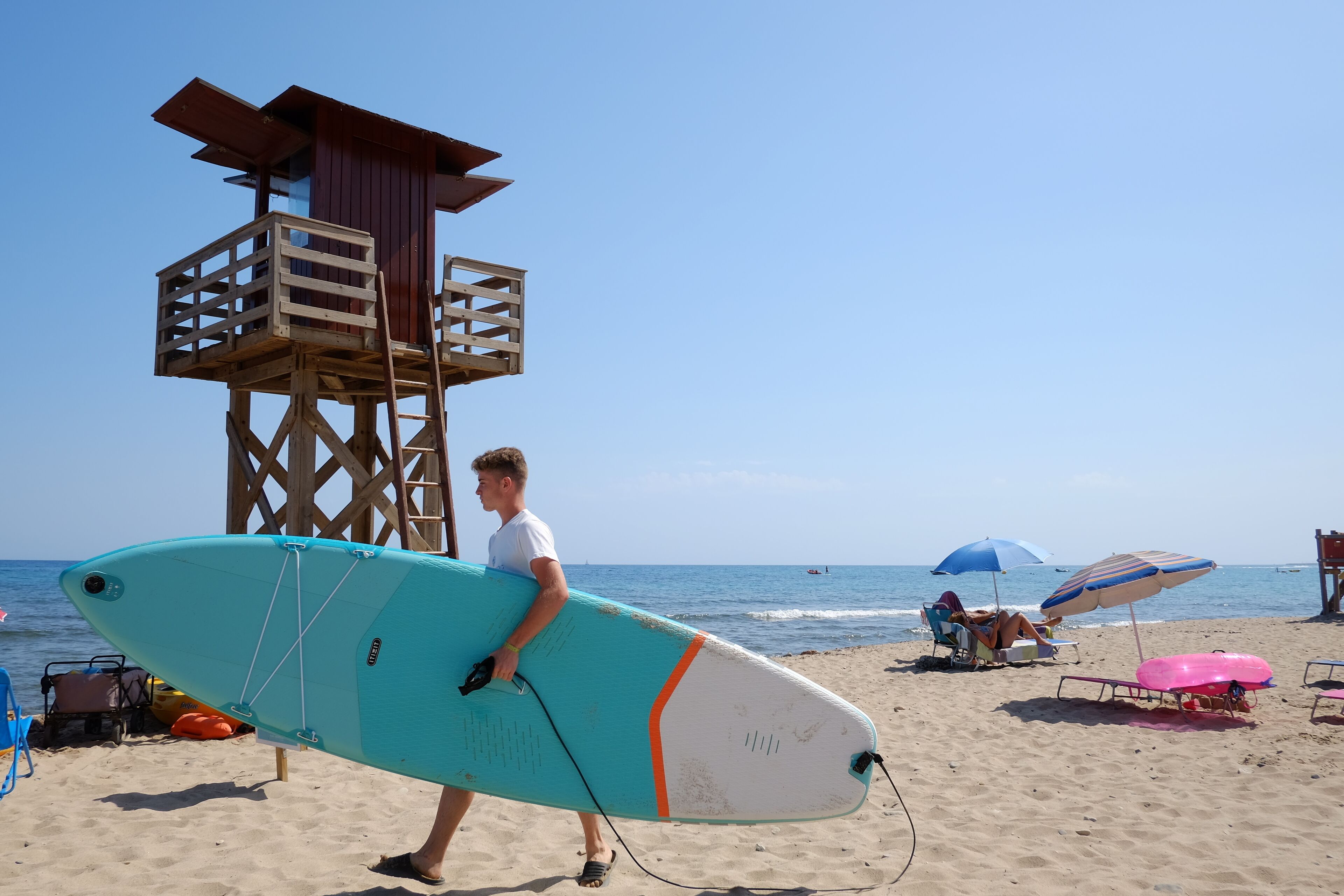 A lifeguard tower, beach chairs, and a surfboard on a sandy beach.