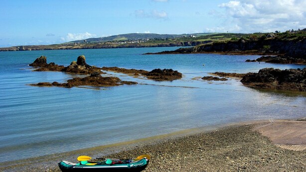A kayak on a pebbly beach with calm water and rocky outcrops. - The Anchorage (Amlwch)