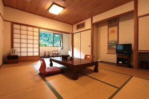 Une pièce de style japonais traditionnel, avec un sol recouvert de tatamis, une basse table en bois, un téléviseur et des portes coulissantes.
