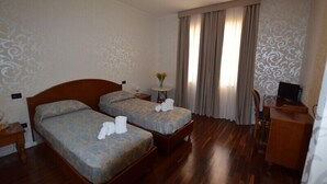 Habitación de hotel con dos camas, un escritorio, una silla, un televisor y una ventana con cortinas.