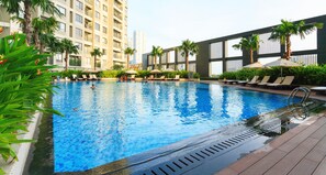 A swimming pool with lounge chairs and umbrellas, surrounded by palm trees and modern buildings.
