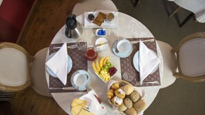 Ein Frühstückstisch für zwei Personen, gedeckt mit Tellern, Tassen, einem Saftkrug, einer Obstschale und verschiedenen Gebäckstückchen.