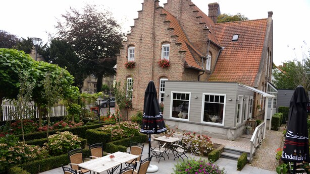 Ein Innenhof mit Außenbestuhlung, ein Backsteinhaus und ein kleiner Garten.