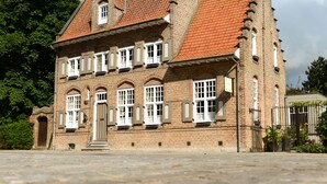 Ein historisches Backsteingebäude mit Ziegeldach, mehreren Schornsteinen und einem zentralen Eingang mit Tür und Fenstern.