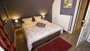Ein Schlafzimmer mit einem Bett, zwei Nachttischlampen, einem roten Teppich, einer Tür und einem Bild an der Wand.
