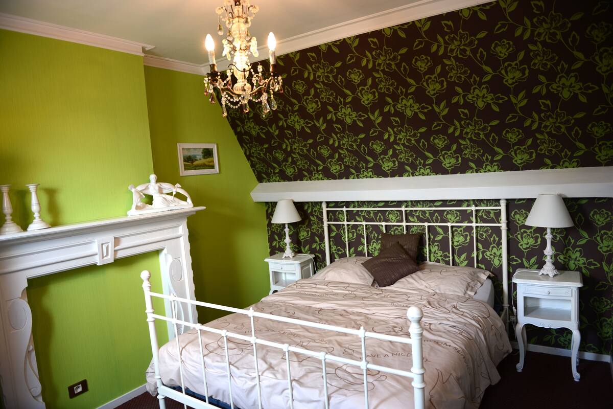 A bedroom with a white four-poster bed, green walls, and floral wallpaper.