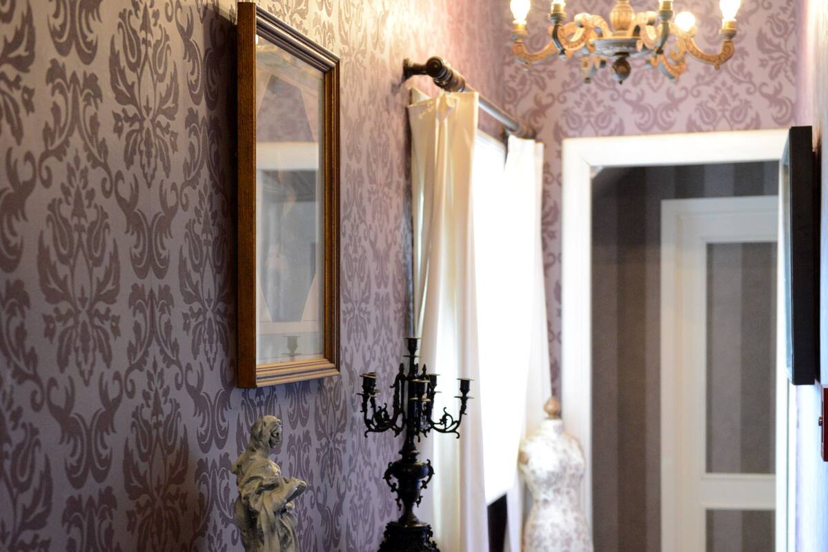A hallway with patterned wallpaper, a wooden console table with a statue, a candelabra, and a red patterned rug.