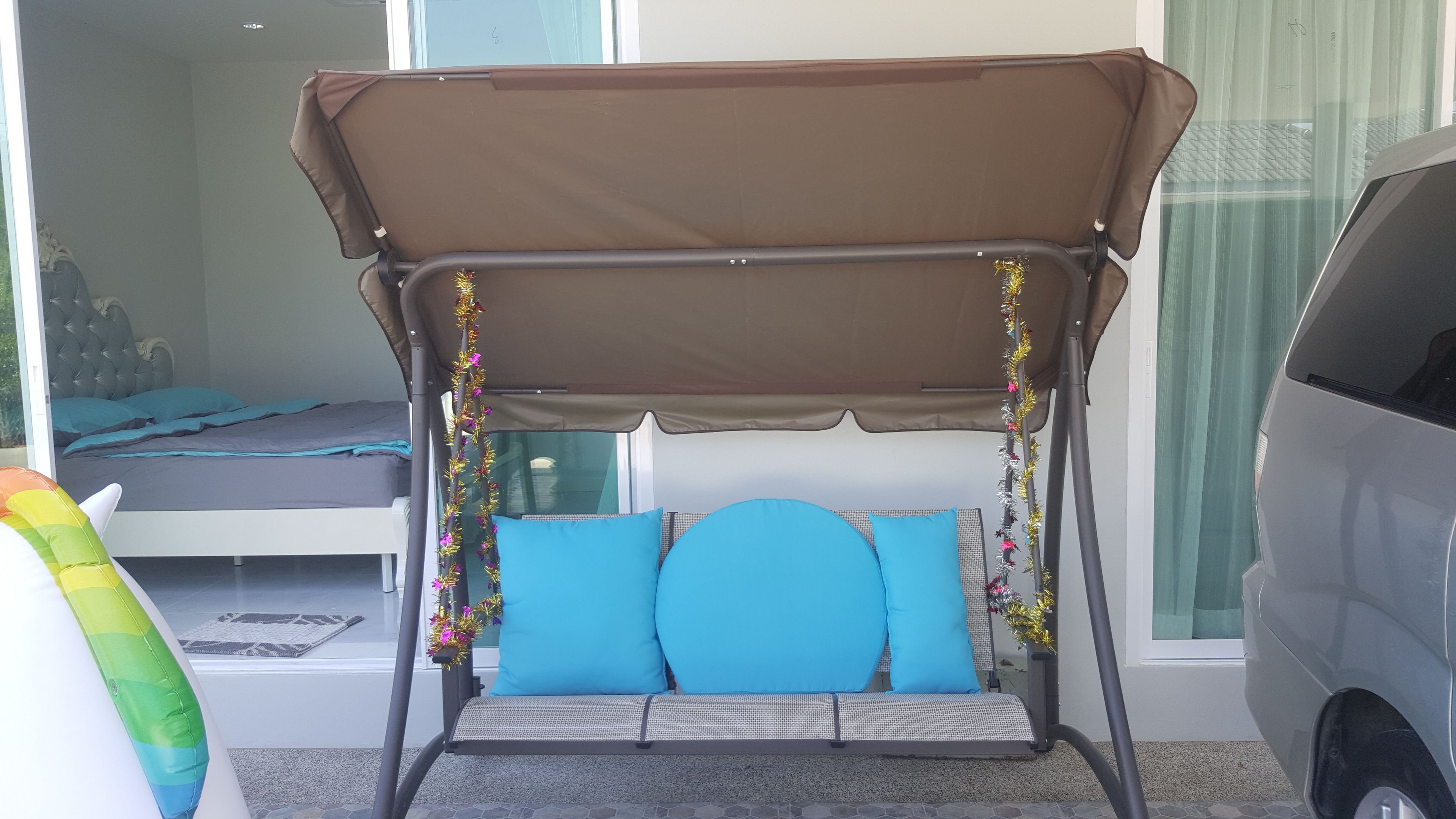 A room with a swing chair, a bed, and a car parked outside.