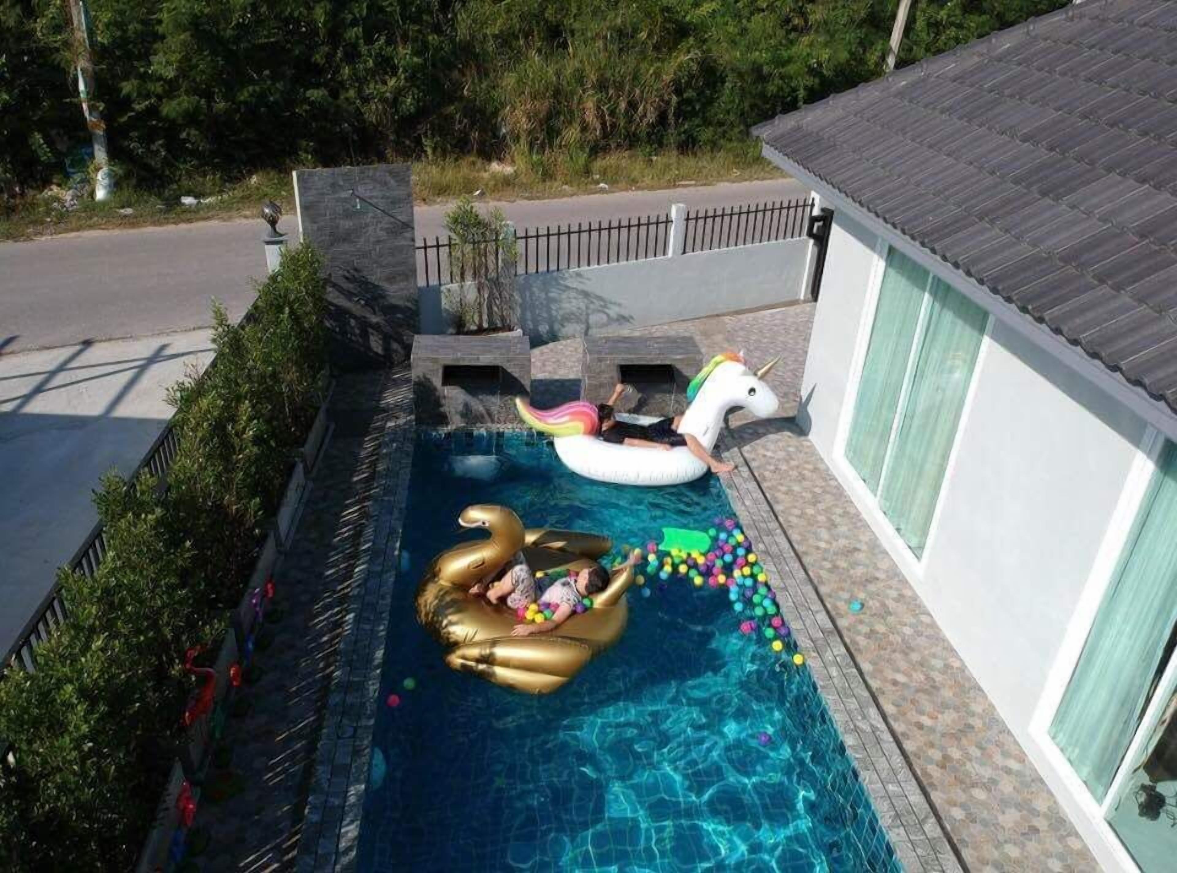 Ein Swimmingpool mit Schwimmreifen in Form eines Schwans und eines Einhorns, umgeben von einem Zaun und einem Haus.