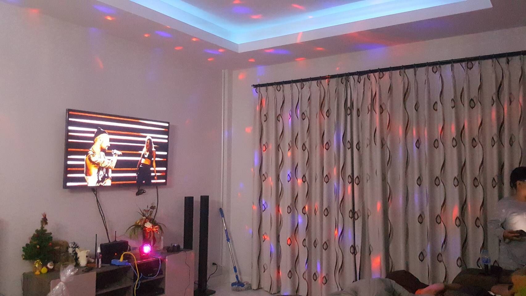 A living room with a flat-screen TV, a Christmas tree, and a curtain with a wavy pattern.