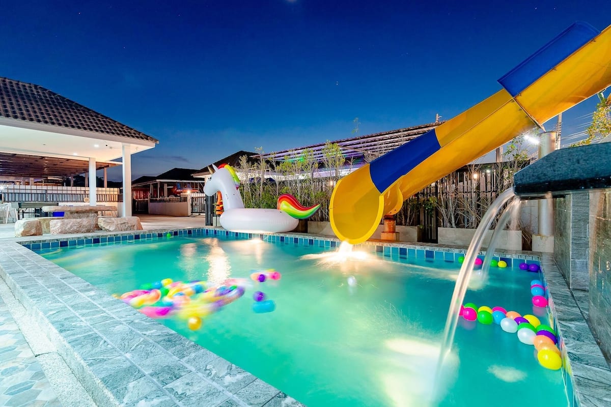 A pool area with a water slide, inflatable unicorn, and colorful balls.