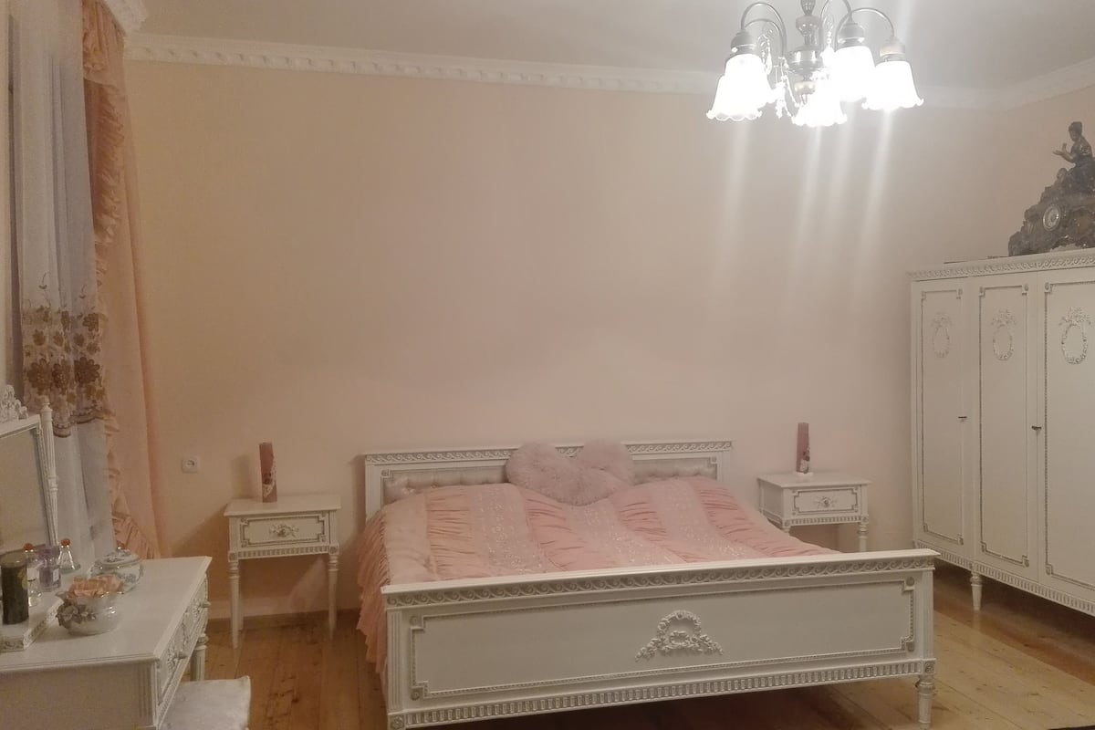 A bedroom with a bed, nightstands, a dresser, and a chandelier.
