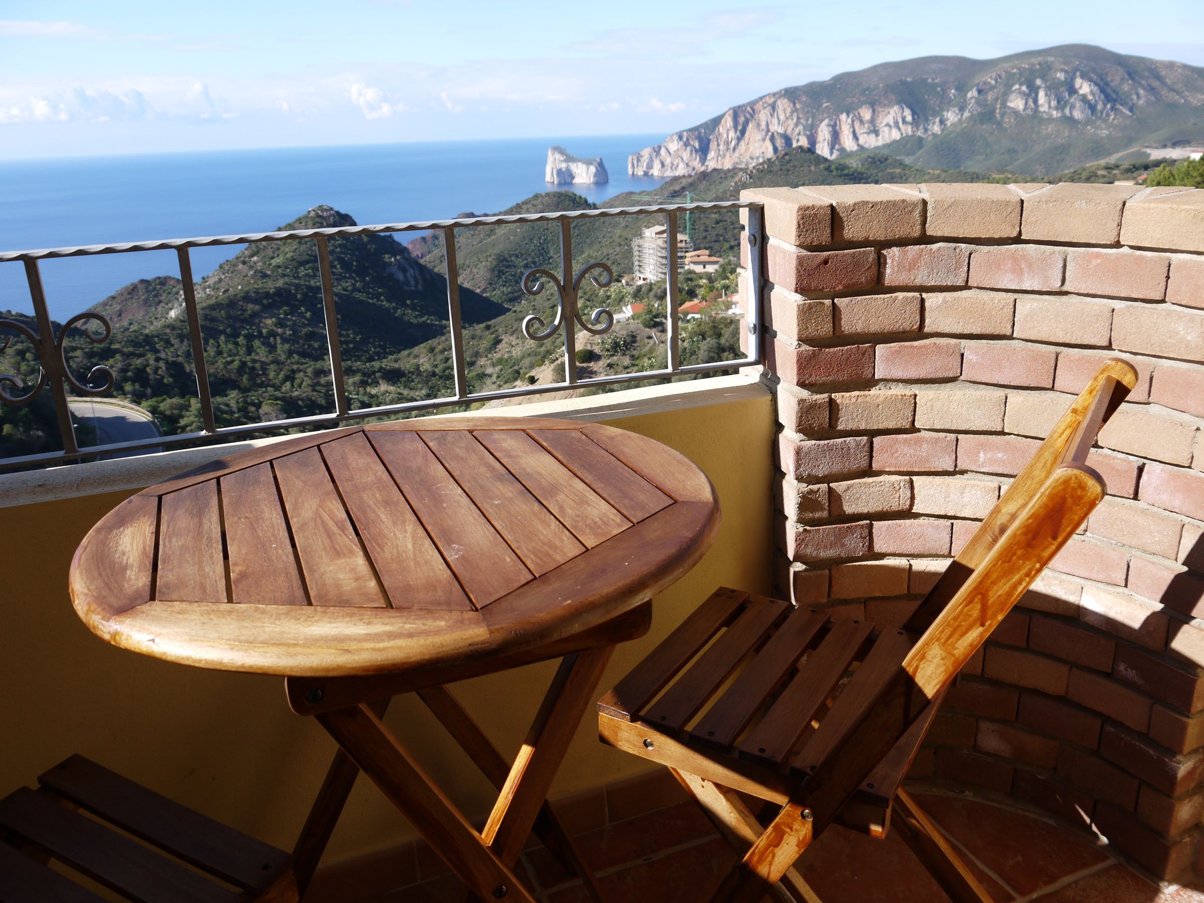 Un tavolo e una sedia in legno su un balcone con vista sul mare e sulle montagne.