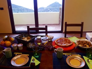 Una mesa de comedor dispuesta con platos, tazones y cubiertos, con vistas a montañas a través de una ventana.