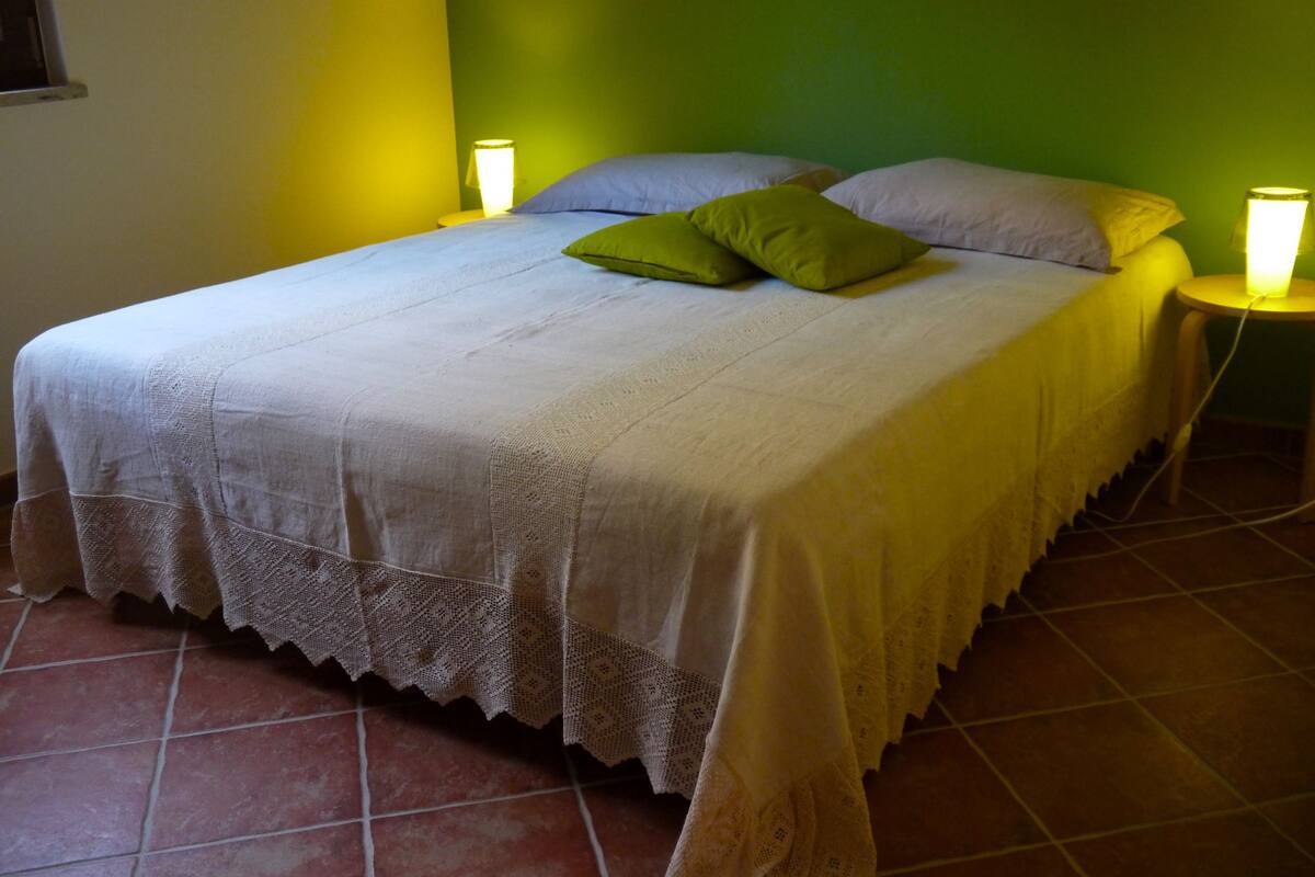 A bed with a white bedspread and green pillows, two bedside lamps, and a green wall.