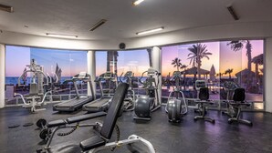 A gym with various exercise equipment and large windows offering a view of the beach at sunset. - Luna Blanca 0801-2BR by Kivoya (Puerto Peñasco)