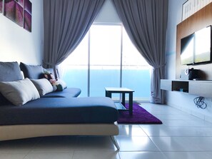 Een moderne slaapkamer met een bed, een klein tafeltje, een televisie en een uitzicht op de lucht door grote ramen.