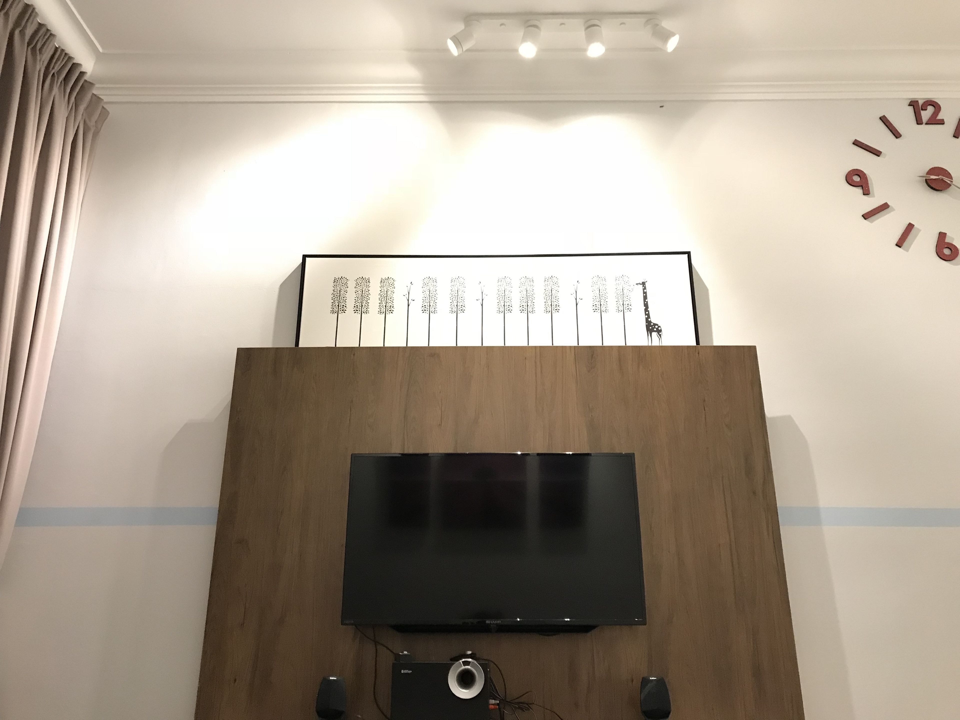 A modern living room with a flat-screen TV mounted on a wooden cabinet, a framed artwork above the TV, and a wall clock.