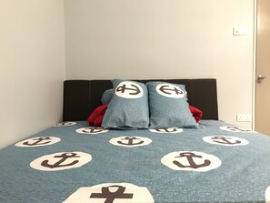 A bed with a blue blanket featuring anchor patterns, a dark headboard, and a red pillow.