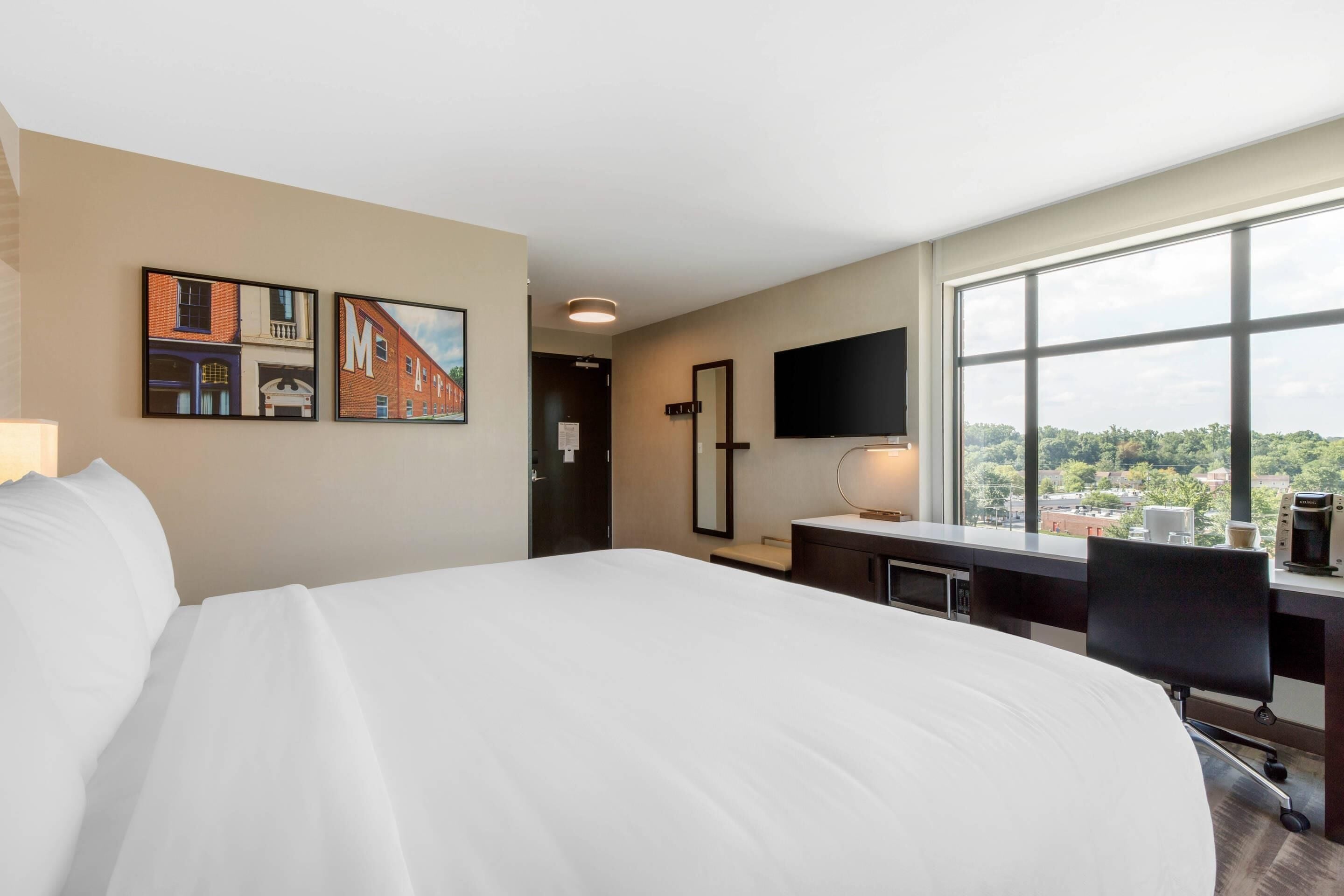 Une chambre d’hôtel avec un grand lit, un bureau avec un ordinateur, une télévision et une fenêtre donnant sur la ville.