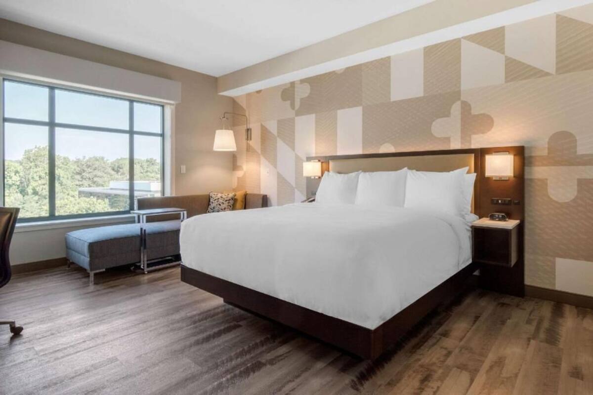 A modern hotel room with a large bed, bedside lamps, a small desk, and a window with a view.