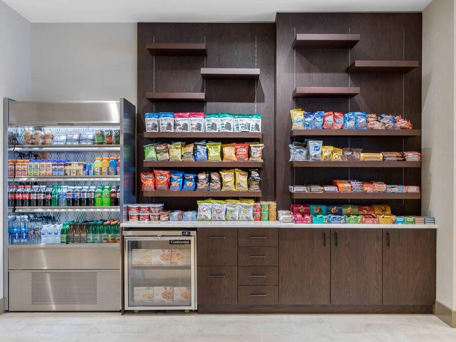 A self-service snack and beverage kiosk with refrigerated drinks, a small refrigerator, and shelves stocked with snacks and packaged goods.
