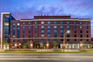 A multi-story hotel with a prominent entrance, a flag, and a sign for the College Park Grill. - Cambria Hotel College Park (College Park)