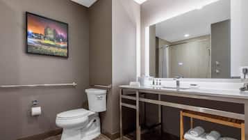 Un baño moderno con inodoro, lavamanos y ducha. Un cuadro enmarco la pared, y hay un perchero con toallas.