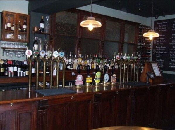 A bar with a variety of beer taps and bottles, wooden cabinets, and hanging lights. - Tulse Hill (London)