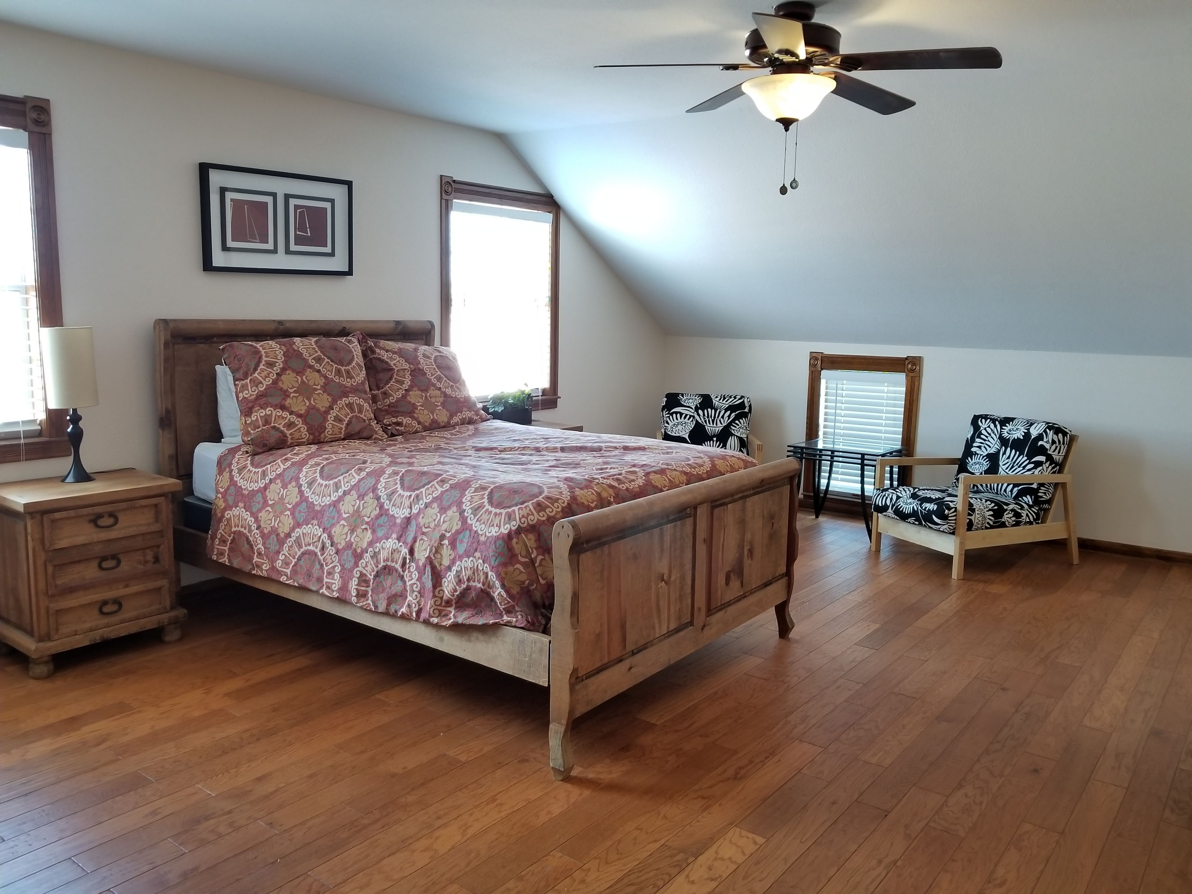 A bedroom with a wooden bed, a ceiling fan, a nightstand, a chair, and a window.