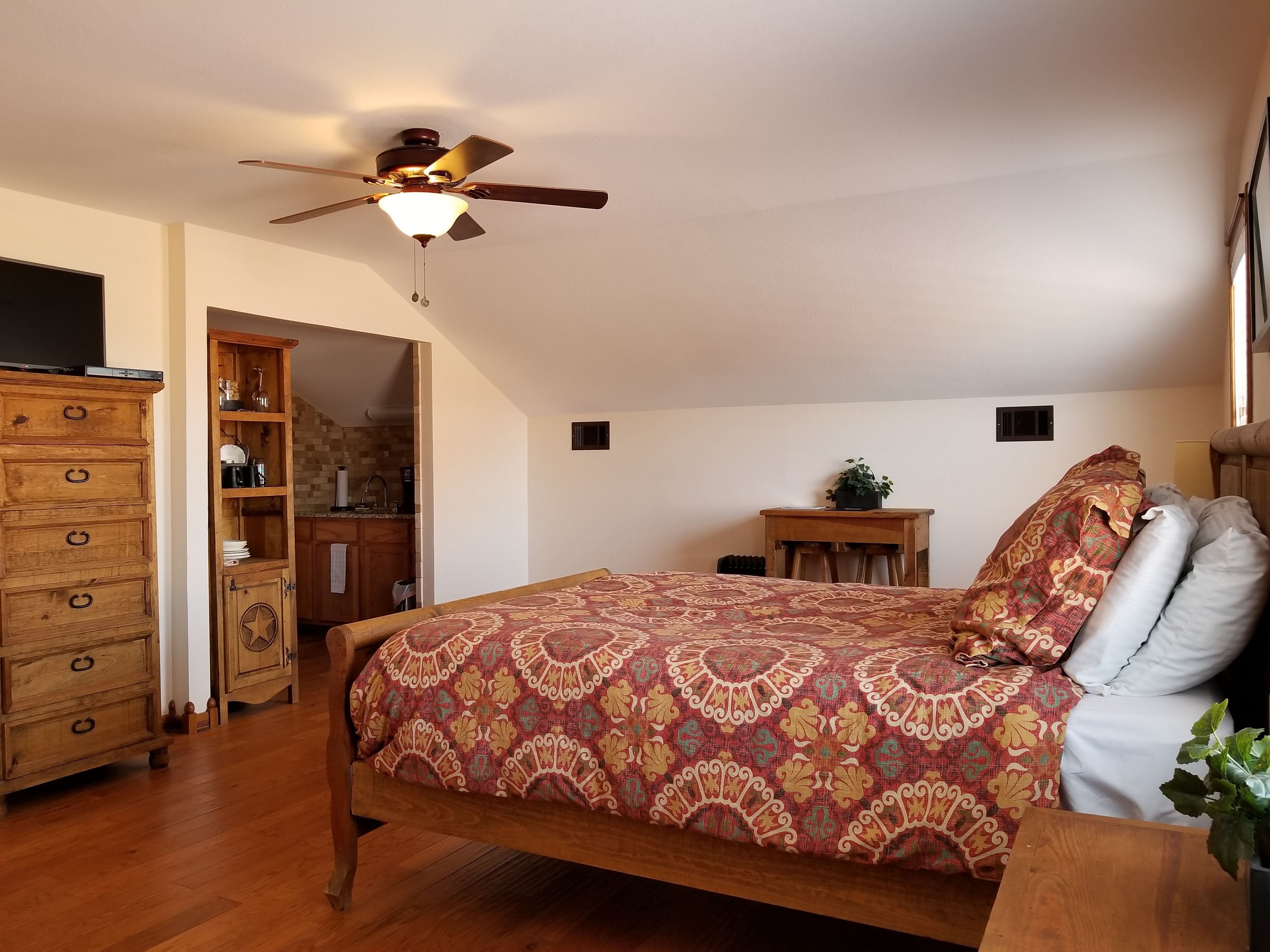 A bedroom with a wooden bed, a ceiling fan, a wooden dresser, and a small table with a plant.